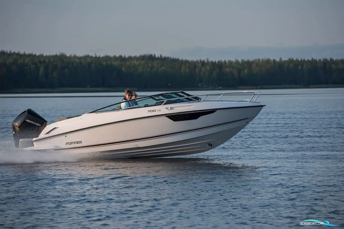 A white Flipper 700 DC boat with two passengers accelerates on calm water, surrounded by lush green trees in the background.